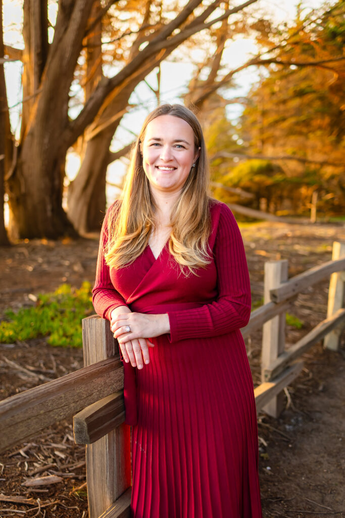 Senior girl wearing a red dress standing on a wooden bridge surrounded by autumn colors