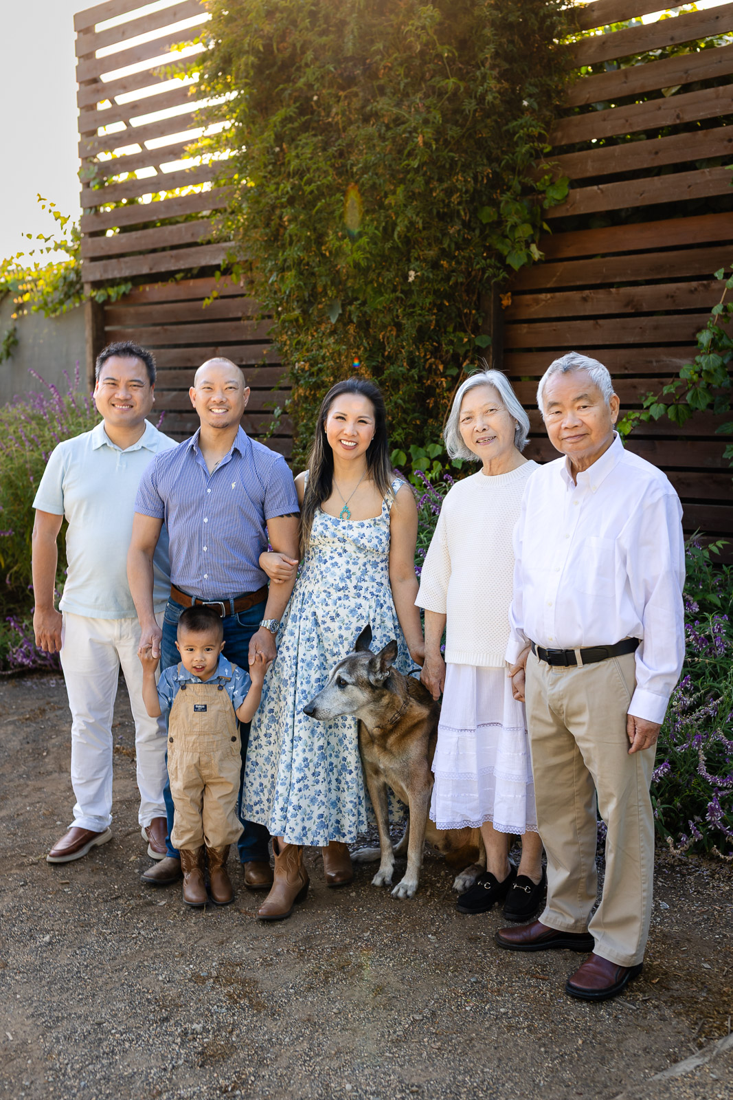 Three-generation extended family posing outdoors in San Mateo County wearing a coordinated white, khaki, and light blue color scheme with their family dog.