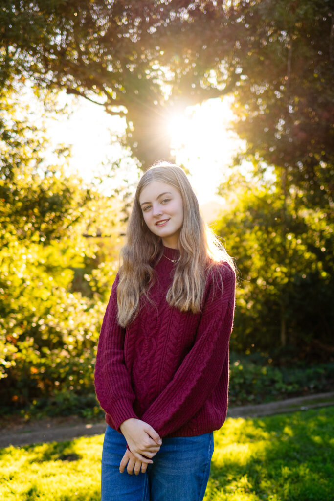 Senior girl smiling in warm evening sunlight surrounded by greenery