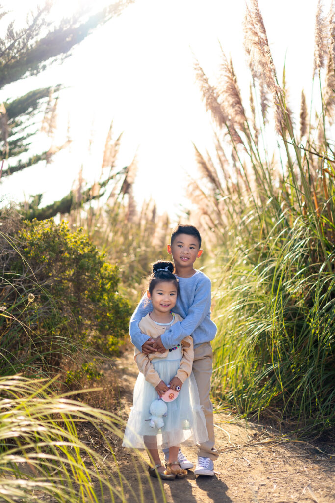 Brother hugging his younger sister in tall golden grasses