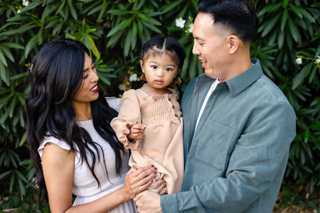 Family of three posing together in a grassy park setting