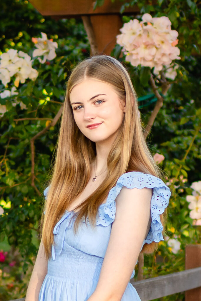 Smiling senior girl in a light blue dress surrounded by blooming flowers