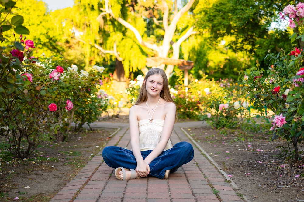 Senior girl sitting on a pathway wearing jeans and a white sleeveless top