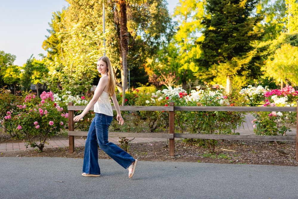 Senior girl wearing jeans and a button-down shirt walking through a garden