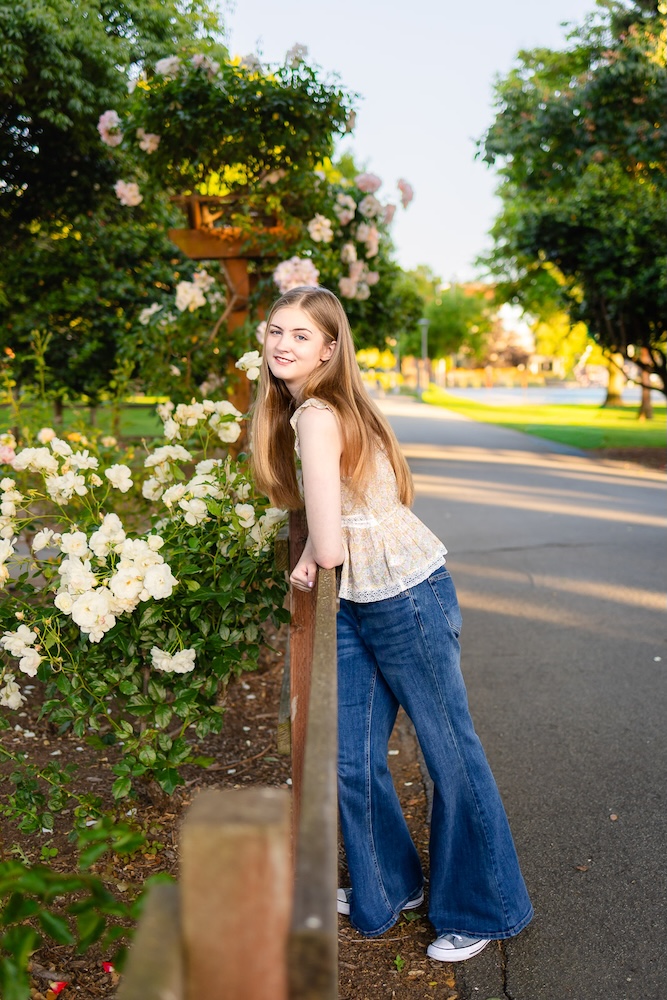 Senior girl wearing jeans and a tank top standing beside flowers in bloom