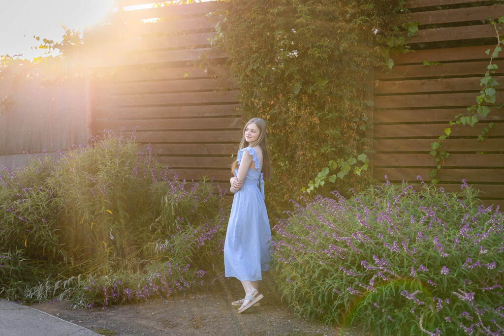 High school senior in a light blue dress standing in a flower garden during golden hour