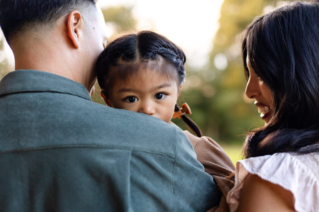 Toddler peeking between parents during a relaxed family portrait session