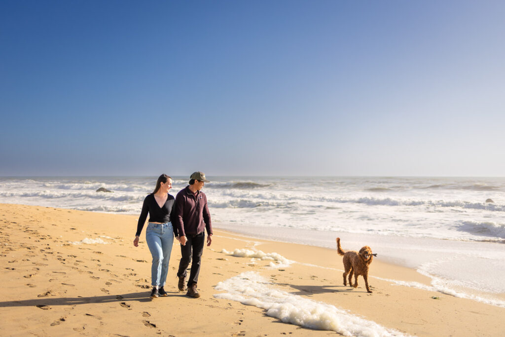 Couple walking with their dog along the shoreline at Half Moon Bay State Beach.