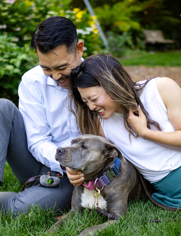 Couple laughing together with their dog during an outdoor portrait session.