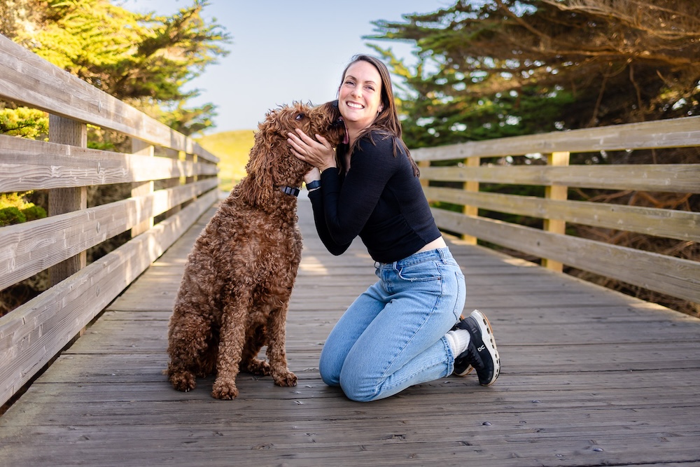 Woman hugging her Labradoodle on a wooden bridge during golden hour.
