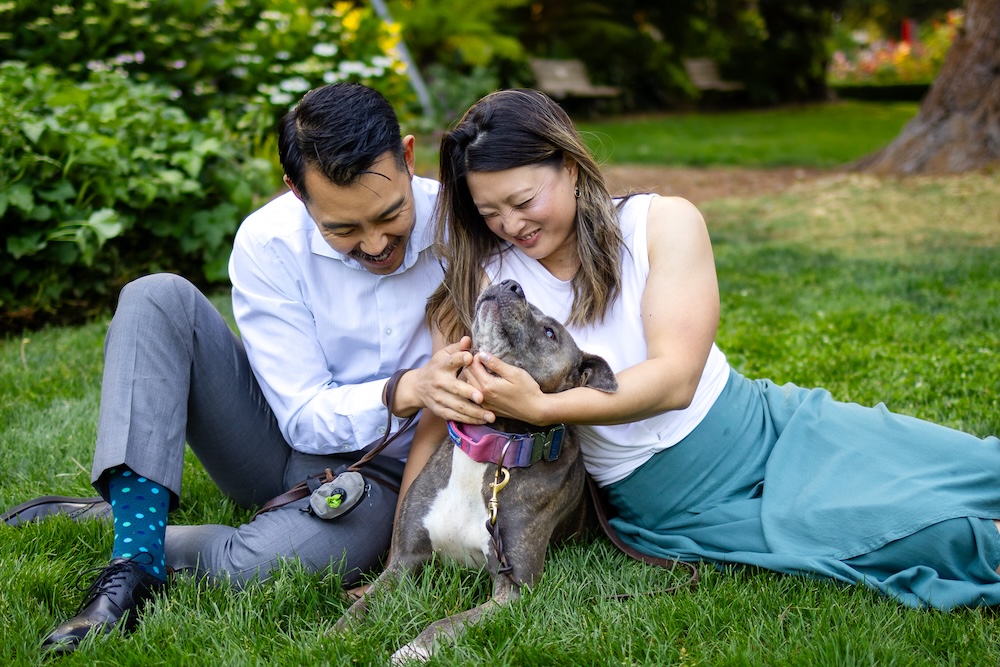 Couple cuddling their pit bull during a playful park portrait session.