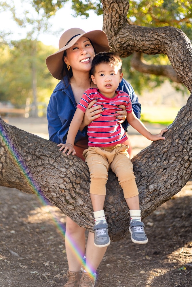 Mom and toddler sitting together in a large oak tree for playful fall picture ideas for family.