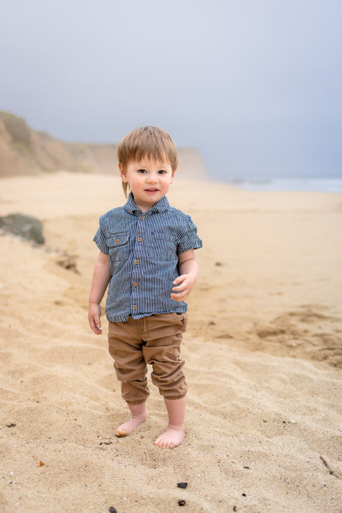 Toddler standing barefoot on the sandy beach during a family photo session.
