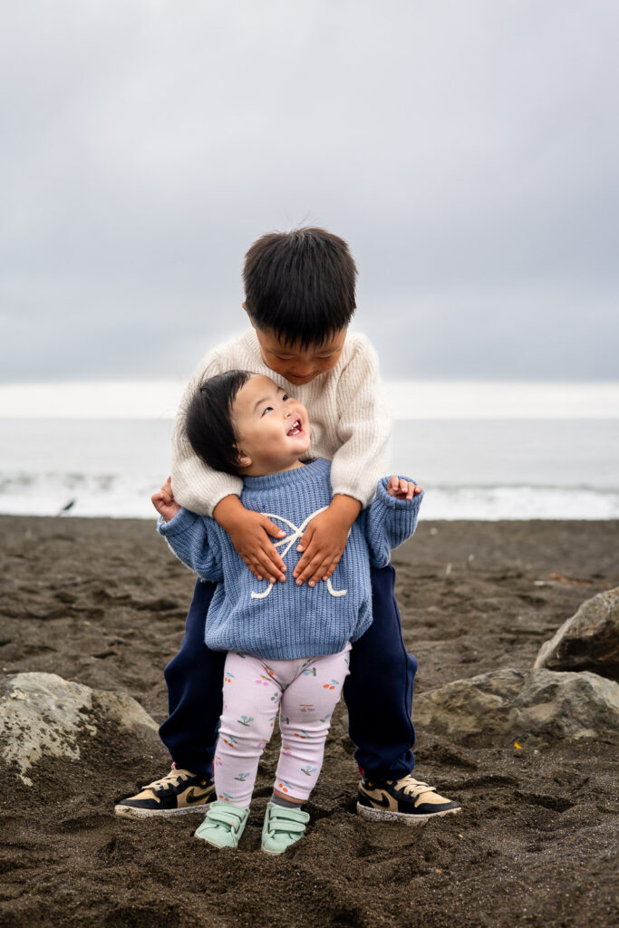 Brother hugging his little sister on the sand at Half Moon Bay State Beach.