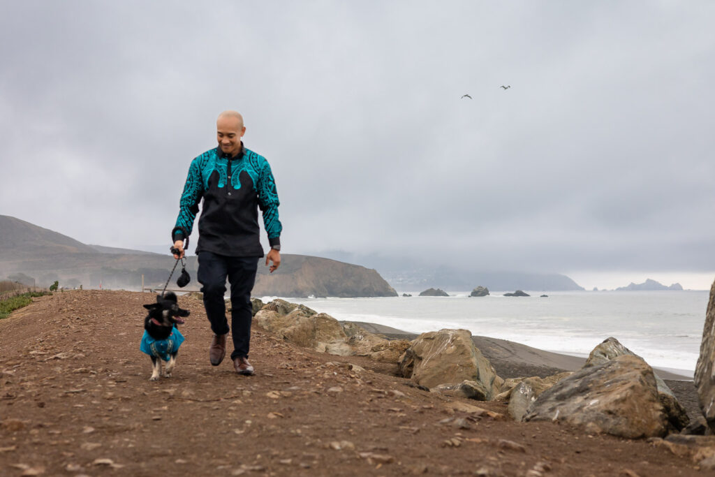 Man walking his dog along Pacifica Beach with dramatic coastal cliffs in the background.