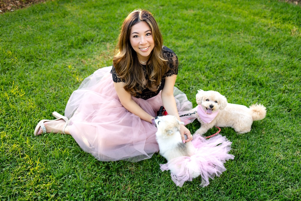 Woman enjoying a playful photo session with dog while posing with two small dogs in a park.