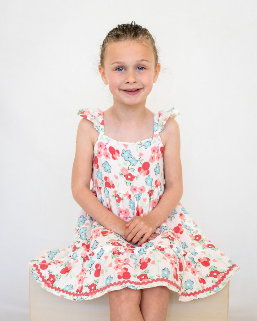 A preschool girl in a floral dress smiles for her school portrait with a San Francisco preschool photographer.