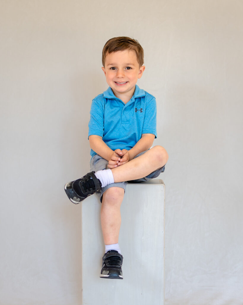 A young boy in a blue polo shirt sits for a classic studio portrait with a San Francisco school photographer.