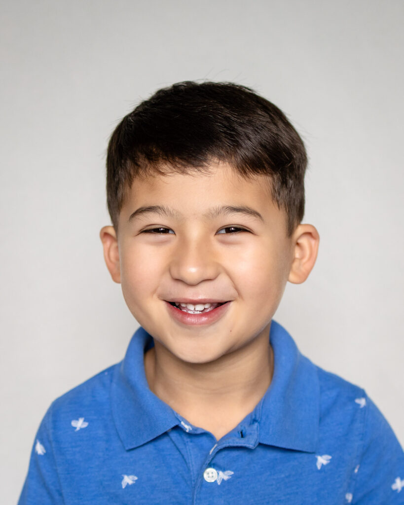 A close-up school portrait of a smiling preschool boy in a blue polo shirt.