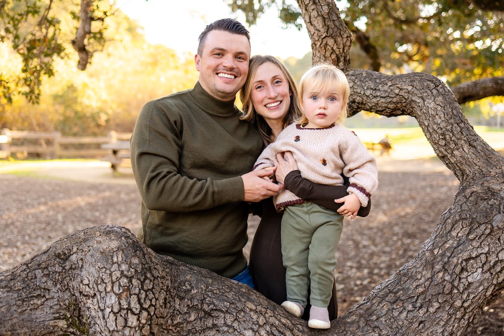 A family of three poses together in the branches of a large oak tree at Laurelwood Park, one of the best San Mateo family photo locations for golden hour light.